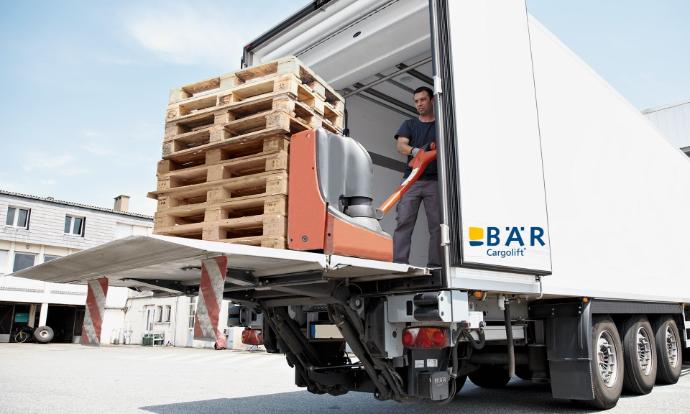 Hayon élévateur rétractable ouvert BAR, sur lequel une personne pousse des palettes vides dans le véhicule