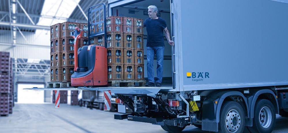 Chauffeur routier déchargeant une palette remplie de boissons et un transpalette électrique équipé d'un hayon élévateur BAR dans un hall