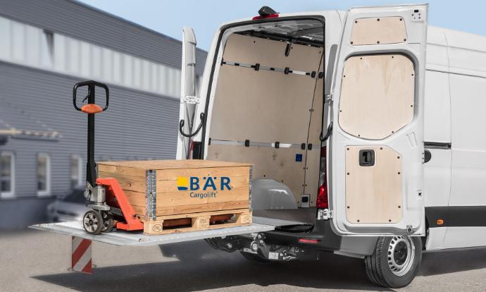 Une palette avec un transpalette se trouve sur la plate-forme dépliée et relevée du Bar VanLift.