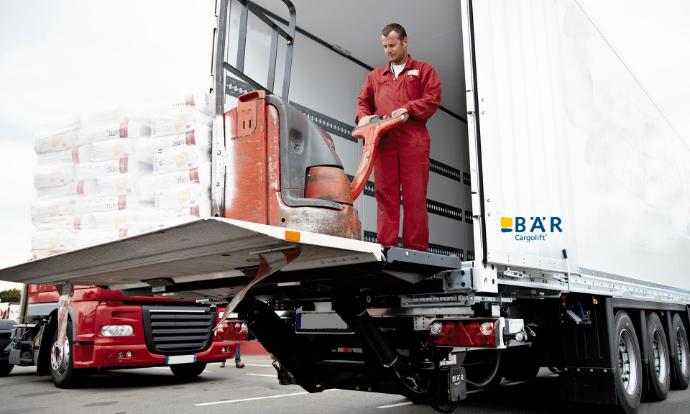 Conducteur avec transpalette électrique et palette lourde sur la plate-forme d'un hayon élévateur Bar