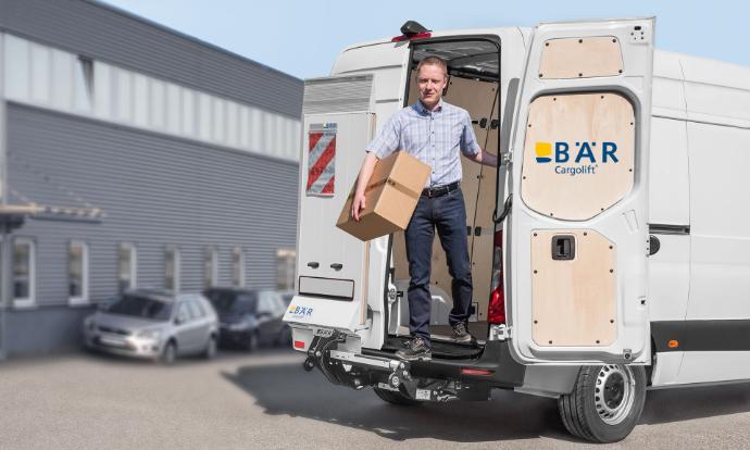 L'homme sort du fourgon avec le colis par la porte arrière tandis que le Bar VanLift FreeAccess reste en position fermée.